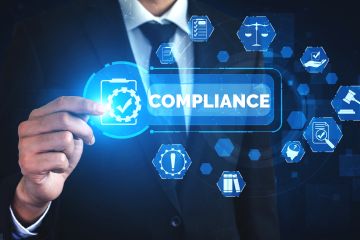 Businessman pointing at a digital compliance icon with law and policy symbols in the background.
