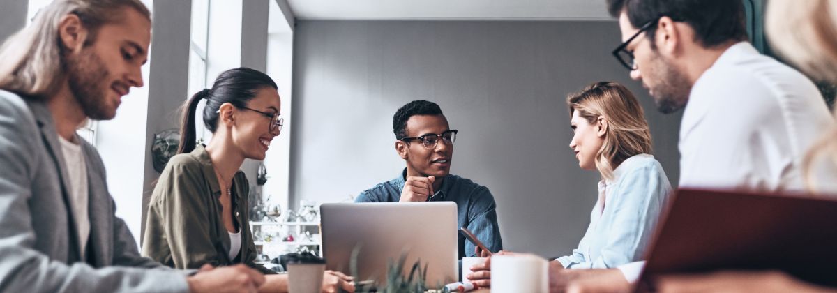 Diverse group of professionals engaged in a discussion around a table in a modern office setting.